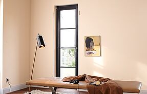 Eine schwarze Stehlampe vor einer Wand in hellem Apricot mit einem dunkelbraunen Sprossenfenster.