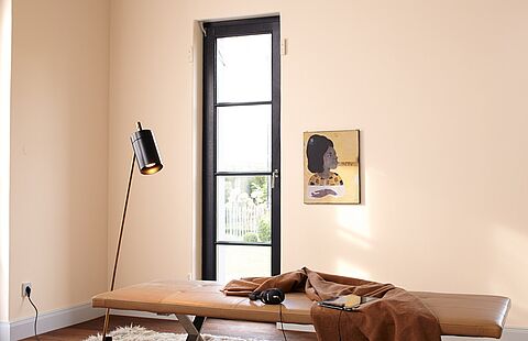Eine schwarze Stehlampe vor einer Wand in hellem Apricot mit einem dunkelbraunen Sprossenfenster.