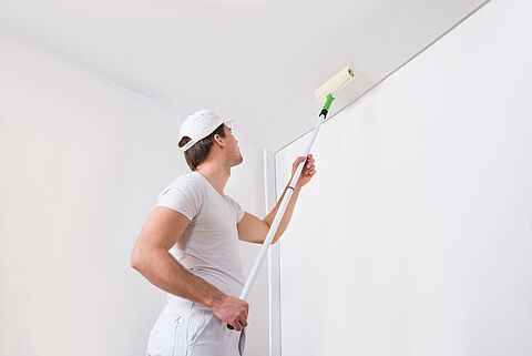 Ein Mann streicht eine Wand mit einem Farbroller und weißer Wandfarbe.