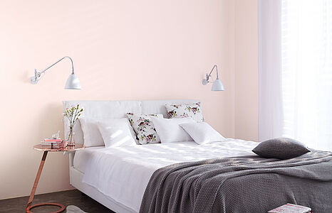 Sanftes Pastellrosé. Ein großes, weißes Bett vor einer in diesem lieblich-grazilen Farbton gestrichenen Schlafzimmerwand.