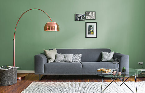 Edelmütiges Patinagrün. Ein in diesem zeitlosen und repräsentativ-eleganten Farbton gestrichenes Wohnzimmer mit grauer Couch.