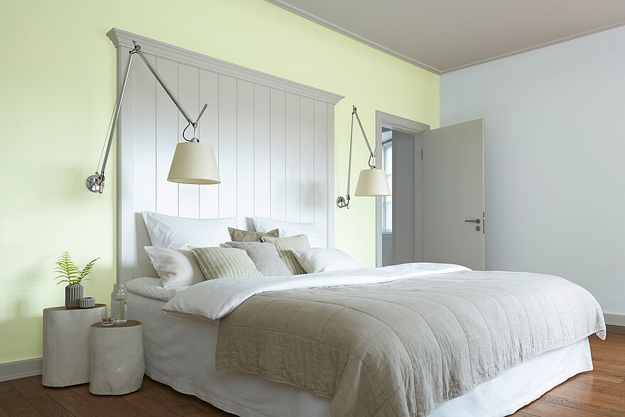 alpina-artikel-passende-wandfarbe-fuers-schlafzimmer-header Ein heller Raum mit einem großen Bett vor einer gelben Wand.